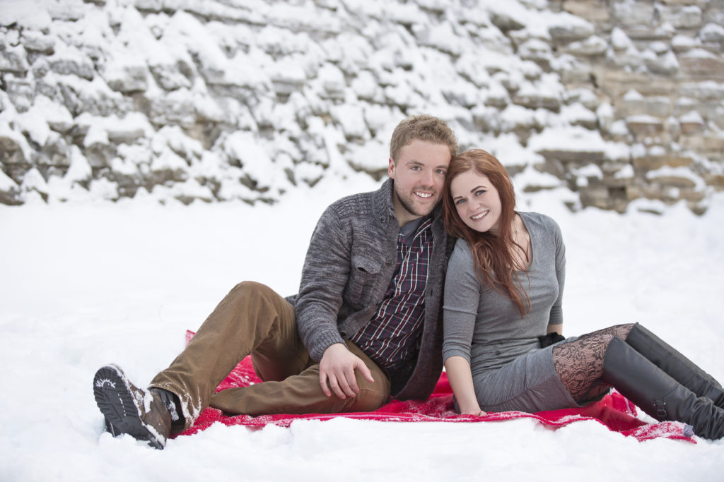 Engaged couple sitting beeing romantic and smiling at their photo session happening during wintertime.